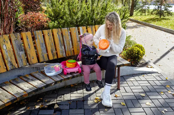 Merhaba Ekim. Anne ve kızı sonbahar şehir parkında yürüyorlar. Ebeveyn ve küçük çocuk dışarıda eğleniyor.