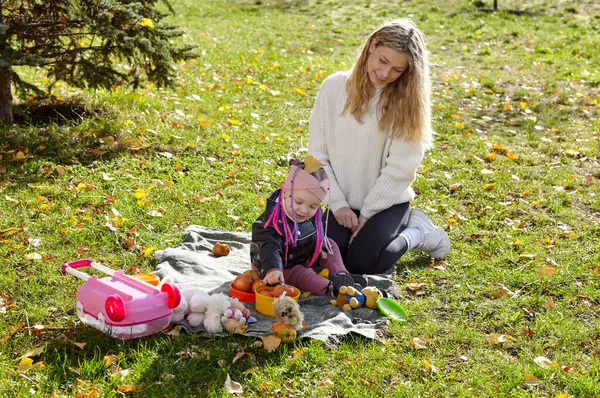 Merhaba Ekim. Anne ve kızı sonbahar şehir parkında yürüyorlar. Ebeveyn ve küçük çocuk dışarıda eğleniyor.