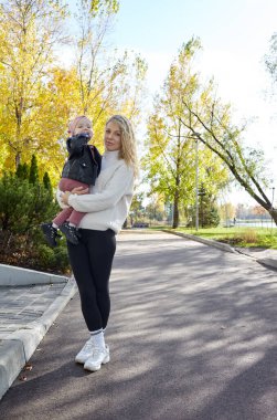 Merhaba Ekim. Anne ve kızı sonbahar şehir parkında yürüyorlar. Ebeveyn ve küçük çocuk dışarıda eğleniyor.