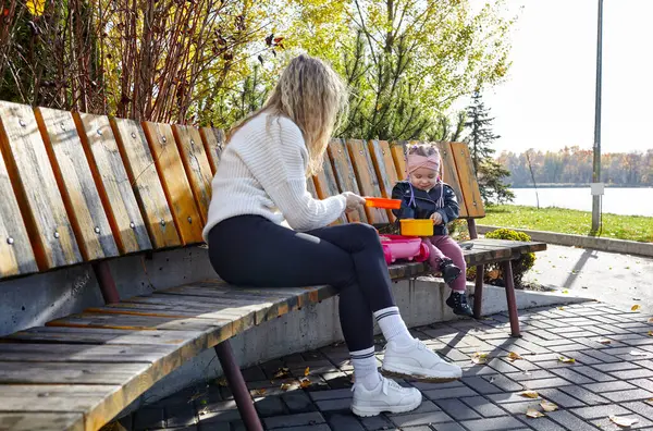 Merhaba Ekim. Anne ve kızı sonbahar şehir parkında yürüyorlar. Ebeveyn ve küçük çocuk dışarıda eğleniyor.