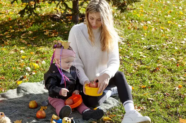 Merhaba Ekim. Anne ve kızı sonbahar şehir parkında yürüyorlar. Ebeveyn ve küçük çocuk dışarıda eğleniyor.