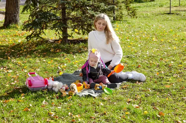 Merhaba Ekim. Anne ve kızı sonbahar şehir parkında yürüyorlar. Ebeveyn ve küçük çocuk dışarıda eğleniyor.