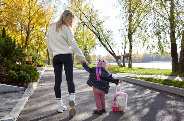 Merhaba Ekim. Anne ve kızı sonbahar şehir parkında yürüyorlar. Ebeveyn ve küçük çocuk dışarıda eğleniyor.