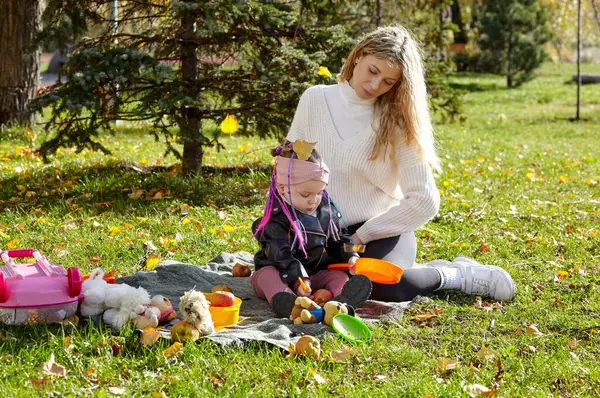 Merhaba Ekim. Anne ve kızı sonbahar şehir parkında yürüyorlar. Ebeveyn ve küçük çocuk dışarıda eğleniyor.