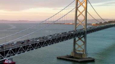 San Francisco City Skyline 'ın ve Bay Bridge' in hava aracı altın güneş ışığı altında. 4K insansız hava aracı görüntüleri, sakin mavi suların üzerinden Bay Köprüsü 'nden geçip Kaliforniya, San Francisco' ya gidiyor.