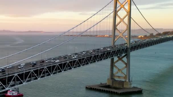 旧金山天际线和海湾大桥的空中无人飞机在柔和的金色日出灯光下飞行 4K无人驾驶飞机拍摄的镜头显示 经过湾桥的车辆在平静的蓝色水面上驶向美国加利福尼亚州旧金山市中心 — 图库视频影像