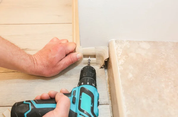 stock image Man is installing the baseboard with a drill. Repair works indoors. Renovation in the flat.