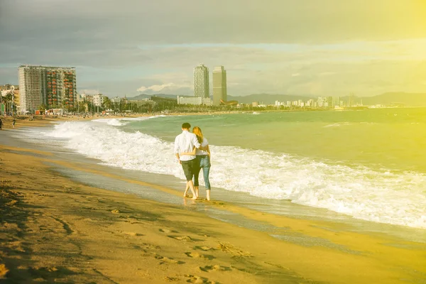 在阳光明媚的日子 夫妻二人在沙滩上散步 时髦的嬉皮士靠近海面上的波浪 男人和女人拥抱和亲吻 Honeymoon 假日旅行的概念 巴塞罗那西班牙的观点 — 图库照片