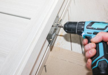 Adam kapıları kuruyor. Marangoz menteşelerde matkapla delikler açıyor. Onarım işe yarıyor. Dairede bakım var..