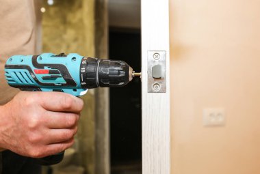 Adam matkapla kapı kolunu kuruyor. Onarım işe yarıyor. Dairede bakım var..