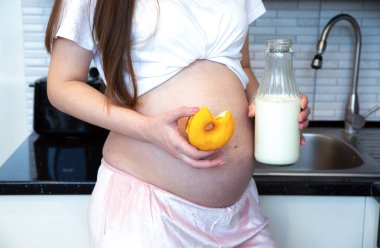 Pregnant woman holding Bottle of milk and Sweet donut. Healthy food during pregnancy.