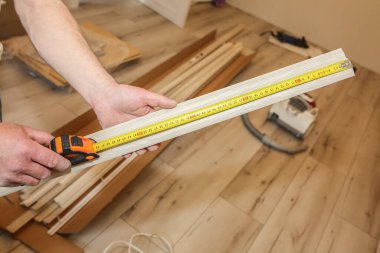 Adam süpürgeliği kuruyor. İçeride tamirat işe yarar. Dairede tadilat var. Elinde mezura var..