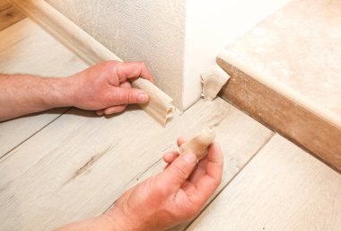 Man is installing the baseboard. Repair works indoors. Renovation in the flat.  Tape measure in hands.