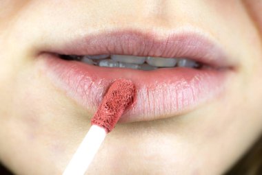 Young woman is doing makeup. GIrl puts on red or pink lipstick. Close up.