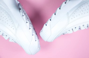 Pembe arka planda modern spor ayakkabılar. Çivili büyük tabanlı beyaz deri ayakkabılar. Kapat..