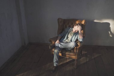 Fotoğraf stüdyosundaki koltukta oturan kot ya da kot elbiseli şık genç adamın portresi..