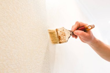 Adam duvara fırçayla yapıştırıcı sürüyor. Duvar kâğıdı asılı. Bakım onarımı dairede tadilat yapıyor. İçerideki restorasyon.