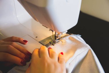 Woman is working at sewing machine. Girls hands with red manicure. Fashion concept. Creating of new clothes process. Hobby ideas.