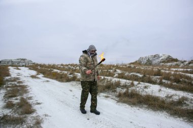 Asker meşaleyi ateşle tutuyor. Kamuflaj üniformalı ve bandanalı bir adam. Dağlarda yaşayan bir adam. Beyaz tepeler ve çöldeki kuru otlar..