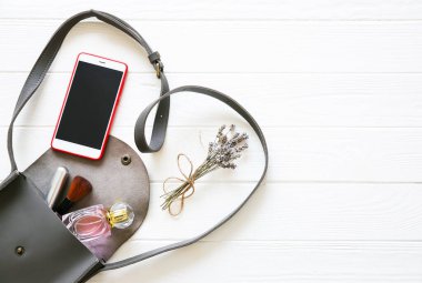 Phone, stylish bag and perfumes on white background. Beautiful flat lay. Things for business woman. Note book schedule. Makeup kit. Lavender bouquet.