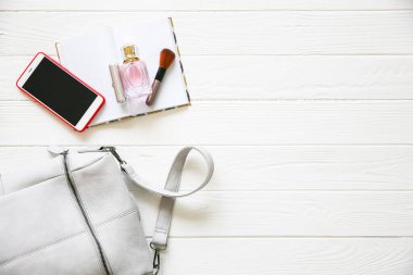 Telefon, şık çanta ve beyaz arka planda parfümler. Güzel düz bir yatak. İş kadını için eşyalar. Not defteri çizelgesi. Makyaj seti.