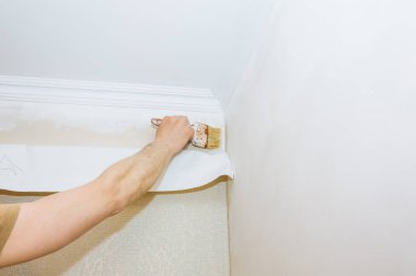 Adam duvara fırçayla yapıştırıcı sürüyor. Duvar kâğıdı asılı. Bakım onarımı dairede tadilat yapıyor. İçerideki restorasyon.