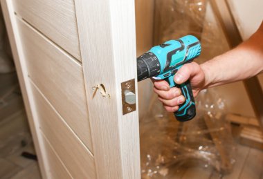 Adam matkapla kapı kolunu kuruyor. Onarım işe yarıyor. Dairede bakım var..