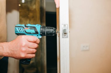 Adam matkapla kapı kolunu kuruyor. Onarım işe yarıyor. Dairede bakım var..