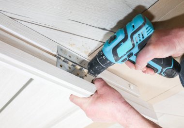 Adam kapıları kuruyor. Marangoz menteşelerde matkapla delikler açıyor. Onarım işe yarıyor. Dairede bakım var..