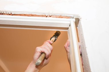 Man installing the doors with a hammer. Holes in the wall. Repair works. Maintenance in the apartment.