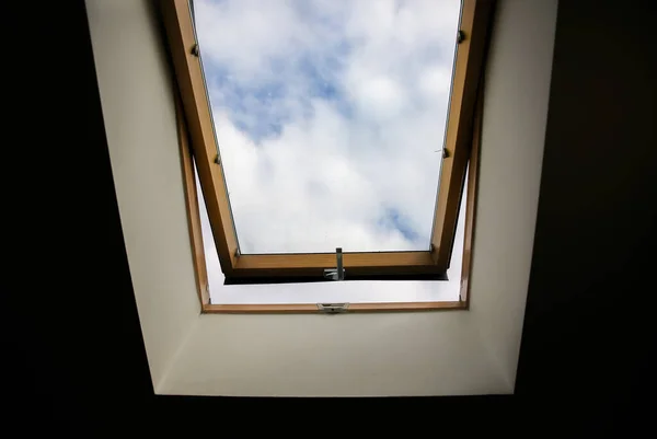 Window in the ceiling. Blue sky with clouds. Attic interior.