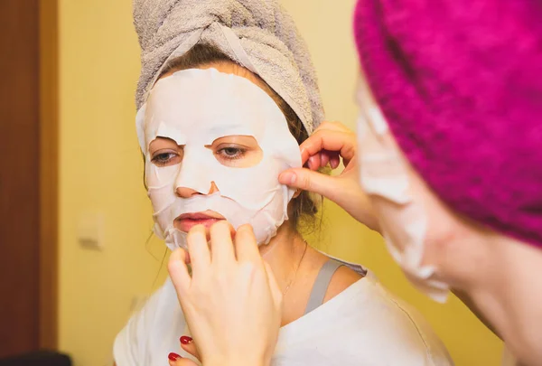 Girls are putting skin mask sheet on face. Beauty procedures at home.