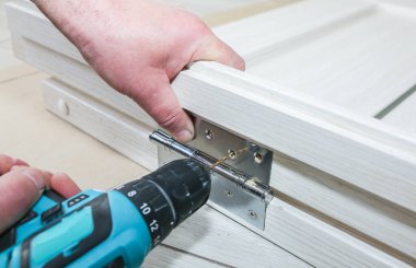 Adam kapıları kuruyor. Marangoz menteşelerde matkapla delikler açıyor. Onarım işe yarıyor. Dairede bakım var..