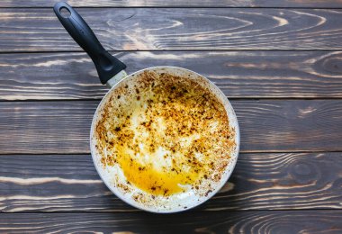 Yağ içinde yanmış tava. Hasarlı mutfak eşyaları. Ahşap arka plan. Sağlıksız yiyecekler.