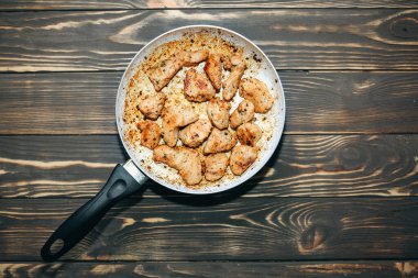 Yağlı ve baharatlı kızarmış tavuk göğsü. Sağlıksız yiyecekler. Yanmış tava. Hasarlı mutfak eşyaları. Ahşap arkaplan.