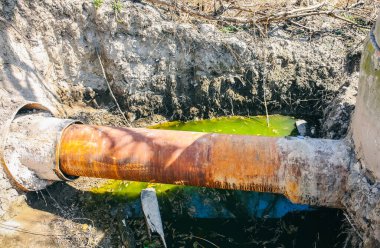 Environment pollution. Old pipe in the field. Green dirty water.