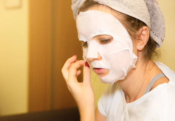 Girl is putting skin mask sheet on face. Beauty procedures at home.