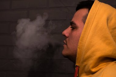 Man is smoking Vape Pod System at home near the gray wall. Electronic cigarette.