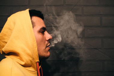 Man is smoking Vape Pod System at home near the gray wall. Electronic cigarette.