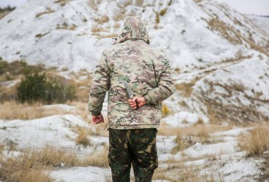 Asker kamuflaj üniforması içinde ve damalı keffiyeh shemagh bandanası içinde duruyor. Bıçaklı adam ıssız bir yerde, dışarıda..