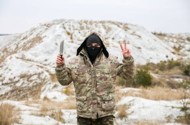Asker, kamuflaj üniforması ve damalı bandana giyiyor. İnsan, terk edilmiş bir yerde, dışarıda. Huzurlu işaret.