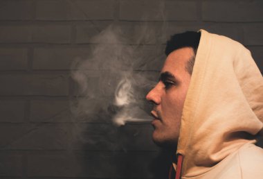 Man is smoking Vape Pod System at home near the gray wall. Electronic cigarette.