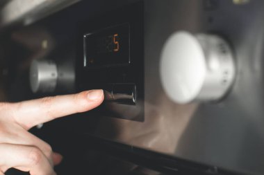 Kadın modern elektrikli fırını mükemmel yemek hazırlamak için zamanlayıcıyla ayarlıyor..