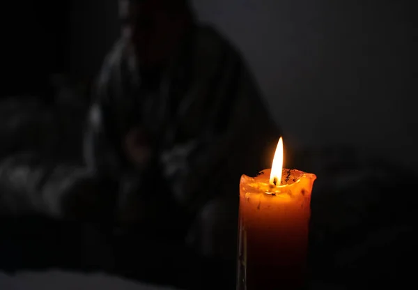 Burning Candle and man in warm blanket. Energy supply problems. Saving electricity concept. Increase in energy bill prices. Cold winter. War in Ukraine. No electricity, blackout concept.