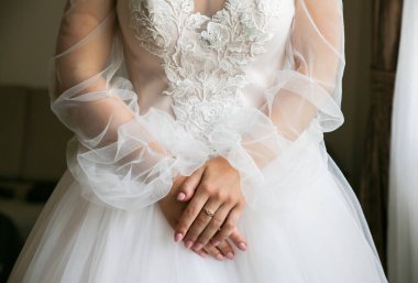Bride is holding her hands on waist. Beautiful long sleeve dress. Lace cloth. Wedding morning details. clipart