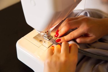 Woman is working at sewing machine. Girls hands with red manicure. Fashion concept. Creating of new clothes process. Hobby ideas.