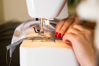 Woman is working at sewing machine. Girls hands with red manicure. Fashion concept. Creating of new clothes process. Hobby ideas.