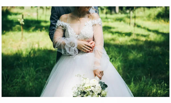 花嫁と新郎が公園で抱き合っている 幸せなカップル一緒に歩いてください 結婚式の日の写真 ラブストーリー 美しい長袖のドレス レースベール スタイリッシュな素朴な花束 — ストック写真