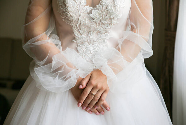 Bride is holding her hands on waist. Beautiful long sleeve dress. Lace cloth. Wedding morning details.