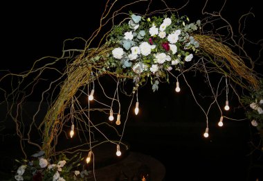 Düğün töreninde beyaz çiçek kemeri. Açık hava dekorasyonu. Romantik köy tarzı. Akşamları lambalar.